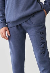 Tmavomodré jogger nohavice vyrobené z jemnej bavlnenej zmesi, so bočnou vreckom a potlačou "BAKER" v čiernej farbe pozdĺž ľavej nohy.