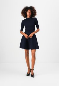Top rigato blu navy con maniche corte e dettagli dorati, abbinato a una gonna svasata blu navy. L'outfit presenta una vita aderente e una texture trasparente.