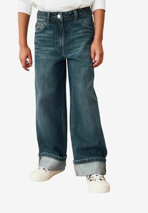 Jeans in denim a gamba larga di colore blu scuro, con vita alta, risvolti e un classico design a cinque tasche. Abbinati a sneakers bianche.