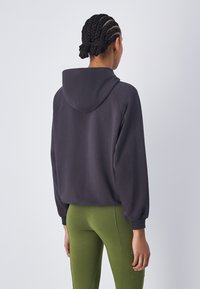 Sudadera con capucha de color gris oscuro, de corte relajado, con puños acanalados y una textura suave, combinada con leggings verdes.