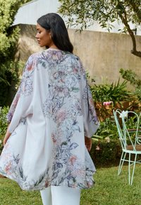 Lightweight floral kimono in pastel colors, featuring a flowy design, wide sleeves, and a soft, textured fabric with a detailed flower pattern.