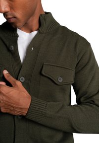 Olive green knit cardigan with a high collar, button closures, and a flap pocket. Features a textured fabric and ribbed cuffs.
