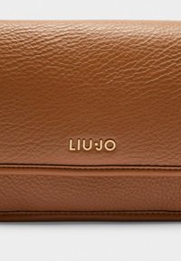 Hnědá texturovaná kožená peněženka se zlatým embosovaným logem "LIU JO", která má hladký vodorovný šev a jemný povrch.