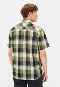 Kortekasmaatschappij met een mix van groen, zwart en crème kleuren, met een knoopsluiting bij de kraag en een ontspannen pasvorm.