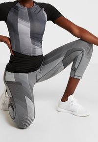 Svart och grått träningsset bestående av en kortärmad, figurnära topp med ett subtilt randigt mönster, samt högmidjade leggings med mönster.