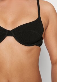 Top de biquíni preto feito de tecido texturizado com um design estruturado, apresentando copas moldadas e alças finas.