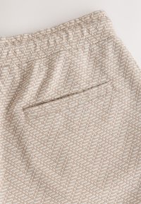 Világos bézs szövött szoknya halszálka mintával és texturált kiemelésekkel. Diszkrét hátsó zsebbel és elasztikus derékrésszel rendelkezik.