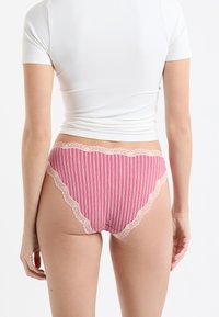 Różowe i białe majtki w paski z koronkową lamówką, o wysokim stanie i miękkiej fakturze tkaniny. Widok od tyłu.