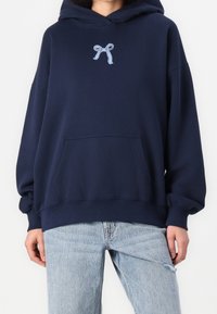 Marinblå hoodie med en framficka, prydd med en ljusblå ribbade brodyr på bröstet, tillverkad av bomullsblandat material med långa ärmar.