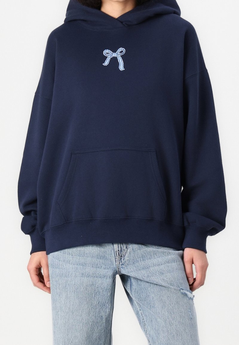 Marinblå hoodie med en framficka, prydd med en ljusblå ribbade brodyr på bröstet, tillverkad av bomullsblandat material med långa ärmar.