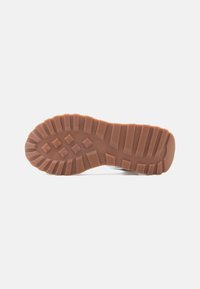 Semelle en caoutchouc marron d'une chaussure avec des crampons profonds et des motifs en forme de croix sur un fond blanc, indiquant la pointure 37.