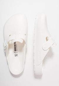 Zuecos blancos con correa ajustable, hechos de material suave. Presentan una plantilla contorneada y una suela texturizada para mayor agarre. Talla 41 marcada en el interior.