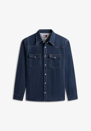 Granatowa dżinsowa koszula z długim rękawem, zatrzaskami, dwoma kieszeniami na klatce piersiowej z patkami, kontrastującymi przeszyciami i małą markową flagą na prawej kieszeni.