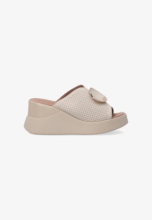Chaussures à enfiler perforées beiges avec une semelle lisse, présentant un bout arrondi et un accent décoratif circulaire sur le dessus.