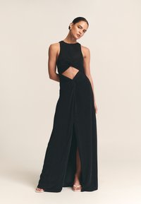 Musta hihaton mekko, jossa kierretty etumalli ja leikkaus vyötäröllä. Mekossa on lattian pituinen helma ja reidestä korkea halkio. Pehmeä pinta.