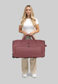 Große weinrote Reisetasche mit zwei Griffen, Reißverschlusstaschen, strukturiertem Oberflächenmaterial und einem Fahrgestell für einfachen Transport.