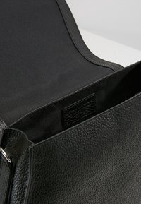 Borsa a mano in pelle nera con esterno texturizzato e fodera interna liscia. Presenta un'apertura superiore e una forma rettangolare.
