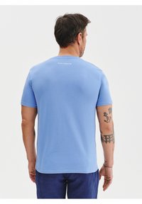Jasnoniebieska koszulka z miękkiego materiału, z okrągłym dekoltem i krótkimi rękawami. Mały detal z logo w białym kolorze na górze pleców.