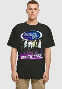 Mustapaita, jossa on värikäs graafinen kuva viidestä hahmosta ja teksti "Backstreet's Back", violettiin korostettuna ja pistekuvioinnilla.