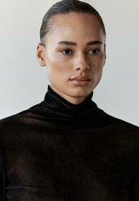 Czarny top z wysokim kołnierzem wykonany z gładkiej, półprzezroczystej tkaniny, o dopasowanym kroju i minimalistycznym wzornictwie, z subtelnymi fałdami i bez widocznych elementów z metalu.