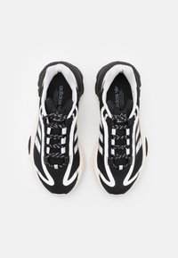 Svartvita träningsskor med en tjock sula, med tre vita ränder, mönstrade snören och en texturerad ovandel.