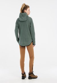 Groene fleece hoodie met een capuchon, lange mouwen en een afgeronde zoom. Gecombineerd met een paarse legging en bruine wandelschoenen. Glad textuur.