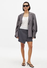 Grå överstor blazer med en knapp, vit linne t-shirt och en grå inslagskjol. Svarta fyrkantiga solglasögon och strappy svarta klacksandaler.