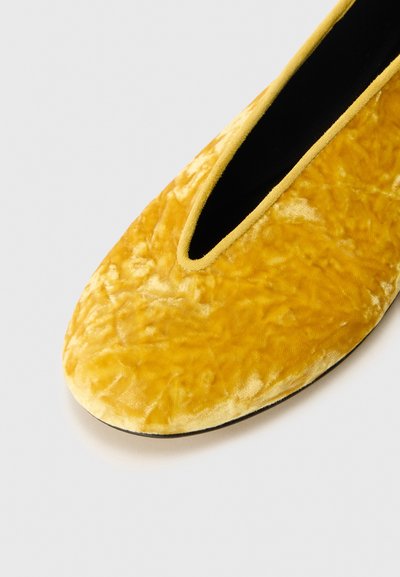 Zapato plano de terciopelo amarillo con punta redonda y un diseño de corte bajo. Textura suave y acabado sin costuras con un interior negro contrastante.