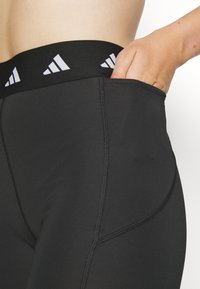 Leggings sportivi neri con un'alta vita, caratterizzati da accenti del logo Adidas bianco, dettagli nelle cuciture laterali e una tasca funzionale. Tessuto morbido e elastico.