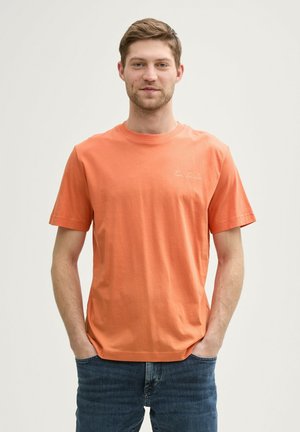 Kortærmet, crew neck t-shirt i strålende orange bomuld. Har broderet tekst på brystet og løs pasform. Båret med blå jeans.