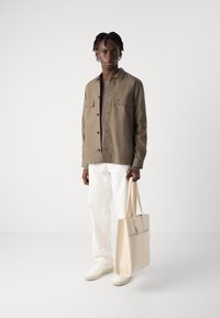 Khaki button-up jacket, white trousers, beige tote bag. Light texture and smooth surface; minimalistic design with a chest pocket.