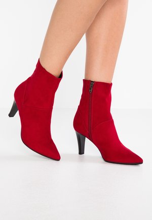 Bottes cheville en daim rouge avec un bout pointu et un talon moyen. Dotées d'une fermeture éclair latérale et de coutures décoratives pour un look ajusté.