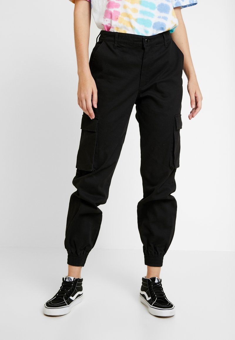 Pantalons cargo noirs avec des poignets élastiques, dotés de poches latérales et d'un design à jambes droites. Associés à des baskets montantes noires.