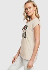 Beige bomulds T-shirt med opsmøgede ærmer, udstyret med et grafisk design af et kranium med blomster og ordet "PALO" i fede, sorte bogstaver.