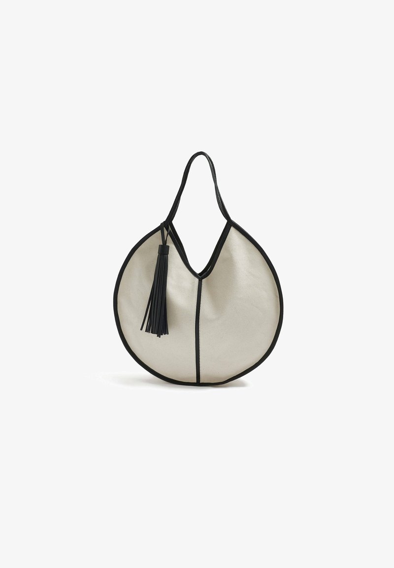 Sac à main en tissu beige avec des bordures et des accents noirs. Présente une forme ronde distinctive et un pendentif noir décoratif attaché à la poignée.