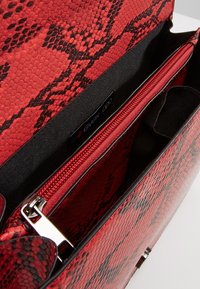 Punainen käärmeenahkakuosinen laukku, jossa sileä pinta. Sisäpuolella vetoketjulla suljettava tasku ja metalliset lukitusosat.