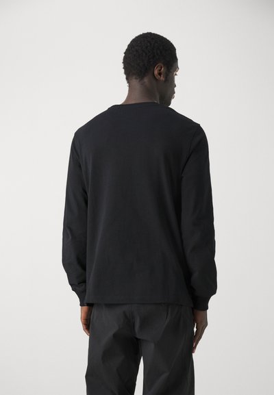 Camiseta de manga larga negra en jersey de algodón. Presenta un cuello redondo y un corte relajado, con puños y dobladillo acanalados. Diseño suave y minimalista.