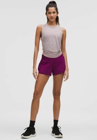 Un haut sans manches rose clair et un short de sport violet. Le short a une taille élastique. Le mannequin porte des baskets noires avec des semelles blanches.