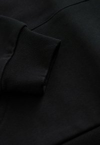 Tessuto di felpa nera con polsini a coste. Texture liscia, leggermente elastica. Il dettaglio mostra le cuciture e l'allineamento delle cuciture.