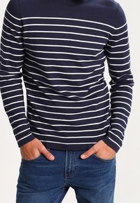 Suéter de manga larga azul marino con rayas horizontales blancas. Cuenta con un cuello redondo y una textura suave. Combinado con jeans de mezclilla azules.