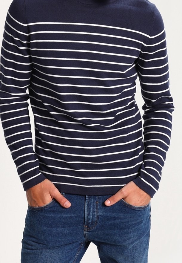 Suéter de manga larga azul marino con rayas horizontales blancas. Cuenta con un cuello redondo y una textura suave. Combinado con jeans de mezclilla azules.