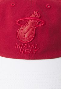 Rød caps med hvit brem, med brodert Miami Heat-logo og tekst. Tøyet er teksturert, og viser et strukturert design med en buet topp.