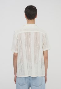 Maglietta a maniche corte, bianca in maglia con un motivo ad apertura simile a pizzo, un design a righe discreto e un colletto, con una vestibilità morbida e un orlo rilassato.