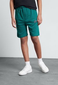 Grønne bomullsshorts med elastisk midje og snøring, med sidelommer og en liten logo, paired med hvite sneakers og sokker.