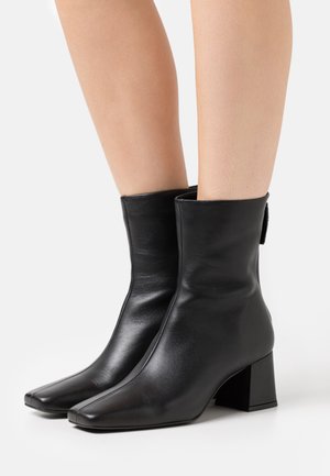 Botines de cuero negro con punta cuadrada y tacón grueso. El diseño presenta una textura suave y un caña de altura media.