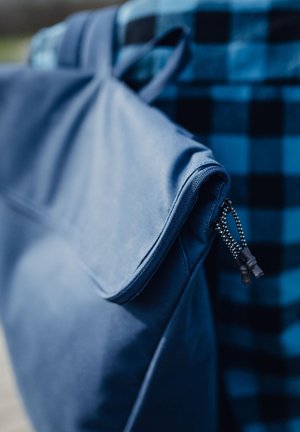 Blue fabric laptop bag with a zippered closure and textured surface, featuring a patterned background in black and blue plaid.
