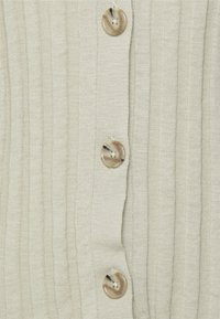 Ljusbeige ribbad kofta med fem rundade, marmorerade knappar; textil med vertikala ränder för extra detaljer.