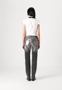 Camisa sin mangas blanca con cuello negro, combinada con pantalones de mezclilla con degradado plateado. Los detalles incluyen dos bolsillos traseros y un cierre con cremallera.