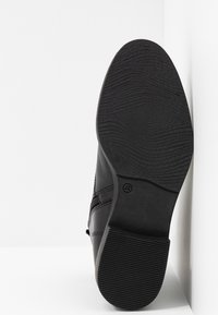 Calzado negro con una suela de goma texturizada, parte superior de cuero suave y costuras decorativas. El tacón mide aproximadamente 3 cm de altura.
