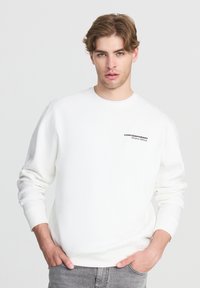 Felpa bianca in cotone con polsini e orlo a coste, caratterizzata da un logo ricamato nero "CONTEMPORARY" sul lato sinistro del petto. Texture liscia.